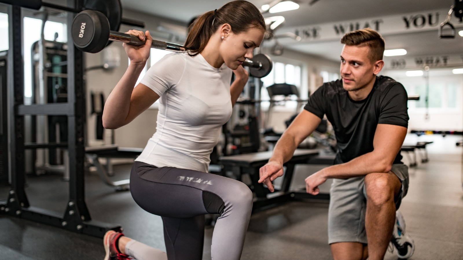 Male personal trainer instructing a female client who is using a barbell